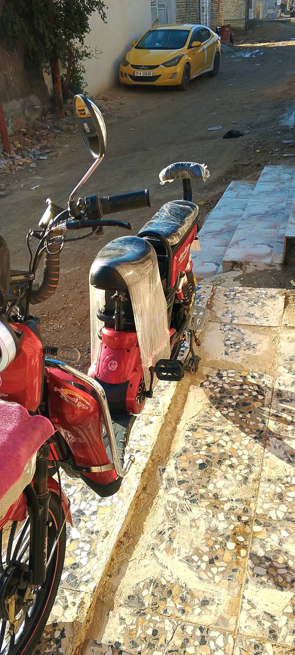 دراجة شحن كهربائية حمراء جديدة مع غطاء حماية على المقعد والمقود. مناسبة للتنقل اليومي داخل المدينة. تمتاز بتصميم عصري ومريح للمستخدم.