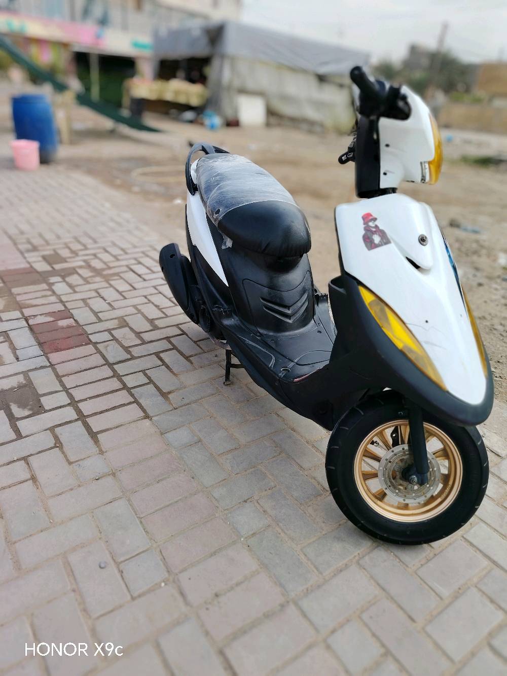 دراجة نارية نوع سكوتر بحالة جيدة للاستخدام، لونها أسود وأبيض مع لمسات ذهبية على العجلات والمصابيح الأمامية.

المزايا:
- تصميم أنيق ومناسب للحركة في المدينة.
- مريحة في القيادة.
- اقتصادية في استهلاك الوقود.

مناسبة للعمل أو للاستخدام الشخصي، متوفرة بسعر منافس.