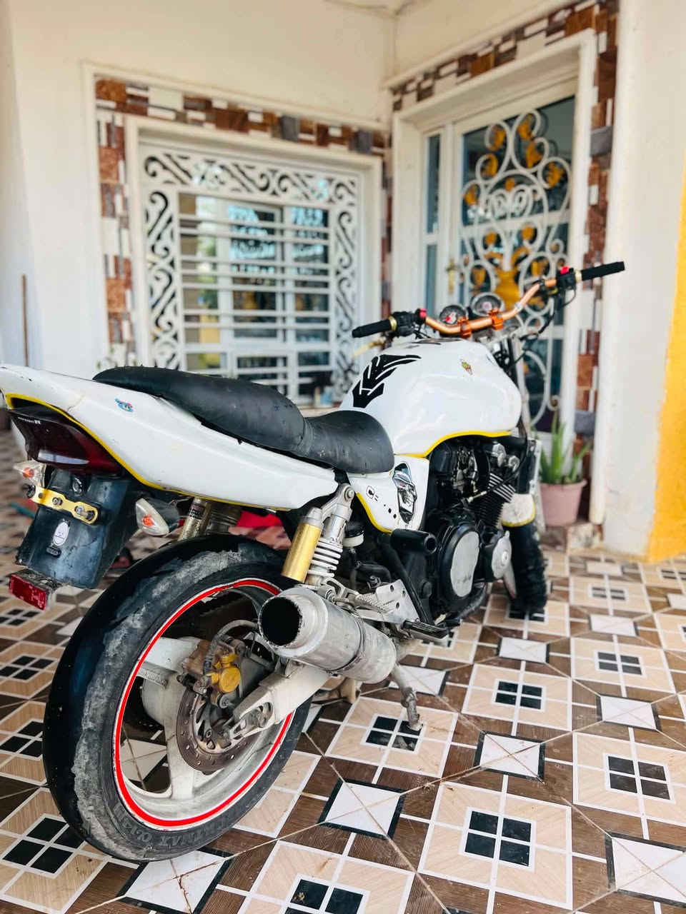 سلام عليكم CB400
هذا الماطور اللي بالصورة هو *هوندا CB400 Super Four*، ويسموه بالعراق "سي بي فور" أو "400 هوندا". وحش ياباني قديم بس بعده هيبة.

### *تفاصيل الماطور من الصورة:*

1. *الموديل*: Honda CB400SF Super Four  
   شكله موديل 1995 - 2003 تقريباً، لأن اللايت الأمامي دائري كبير والعدادات اثنين فوك.
   
2. *المحرك*:  
   - 4 سلندر، 399cc، تبريد ماء.  
   - قوة تقريباً 53 حصان، صوته مميز لأن 4 سلندر.  
   - بي تقنية *VTEC* إذا كان موديل 1999 وفوك، يعني يفتح 4 ولفات إضافية بعد الـ 6300 RPM ويصير صوته يخبل.

3. *الشكل*:  
   - *لون أبيض مع خط أصفر*، بس مبين مصبوغ تعديل مو بلاده.  
   - *لايت دائري كبير* كلاسيكي + ساعتين فوك للعدادات وعليهم ستيكرات.  
   - *راديتر ماء* كدام المحرك، ولذلك حجمه كبير.  
   - *إكزوست معدل*، شكله صوته عالي.  
   - *ويلات بيها خط أحمر*، ودرع الجاملغ الأمامي بي رسمة جمجمة.  
   - *كرسي قطعتين* أسود وأبيض، رياضي.

4. *التعديلات اللي مبينة*:  
   - هاندل بار معدل ذهبي.  
   - كليجات ولايتات إضافية حمر.  
   - ستيكرات على التانكي والجاملغ.  
   - حمالة جانبية للأشياء.

### *مميزاته:*
- *اعتمادي*: محرك الـ 400 مال هوندا يمشيك 100 ألف كيلو إذا تهتم بالدهن.  
- *سريع*: يجيب 180 كم/س مرتاح، والتسارع ماله قوي.  
- *قطع غياره متوفرة* بالعراق نسبياً، خاصة بغداد والبصرة.  
- *وزنه متوسط* 170-180 كغم، يصلح للمبتدئين والخب واسمع صوت الـ VTEC يفتح. وانتبه من الورق مالته لأن هواي تجي تجميع.
متواجد فيس 
رقم الهاتف ***********
رقم الواتساب ***********
سعر الوحش مليون و100وبي مجال لطيبين
