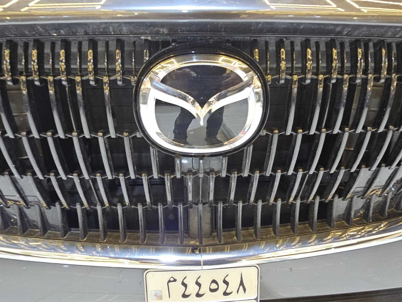 سيارة **مازدا CX-90 موديل 2024** بمحرك الـ 6 سلندر هجين (Mild Hybrid)  حيث تعتمد على محرك طولي ونظام دفع رباعي موجه للخلف لتحقيق أداء رياضي وفخم..
إليك أهم المواصفات التقنية والمميزات:
### 1. المحرك والأداء (e-Skyactiv G)
تتوفر بمحرك 6 أسطوانات متتالية (Inline-6) سعة 3.3 لتر مع شاحن تيربو، مدعوم بنظام هجين بسيط (48 فولت):
 * **القوة الحصانية:** تتوفر بخيارين حسب الفئة:
   * **الفئة القياسية:** 280 حصان وعزم دوران 450 نيوتن متر.
   * **الفئة العالية (S):** تصل إلى 340 حصان وعزم دوران 500 نيوتن متر (وهي أقوى سيارة إنتاجية من مازدا).
 * **ناقل الحركة:** أوتوماتيكي من 8 سرعات (جديد كلياً بدون محول عزم تقليدي لتوفير استجابة أسرع).
 * **نظام الدفع:** دفع كلي للعجلات (i-Activ AWD) بشكل قياسي.
 * **التسارع:** من 0 إلى 100 كم/ساعة في حوالي **5.8 إلى 6.5 ثانية** (حسب القوة).
### 2. استهلاك الوقود
 * تعتبر اقتصادية مقارنة بحجمها بفضل النظام الهجين، حيث تستهلك وسطياً حوالي **9.3 إلى 9.4 لتر لكل 100 كم**.
 * سعة خزان الوقود: **74 لتر**.
### 3. الأبعاد والمساحة
 * **الطول:** حوالي 5.1 متر، مما يجعلها سيارة SUV كبيرة بـ 3 صفوف من المقاعد.
 * **السعة:** تتوفر بخيارات 6 أو 7 أو 8 ركاب حسب التوزيع الداخلي.
 * **مساحة الأمتعة:** 608 لتر (خلف الصف الثالث) وتصل إلى 2025 لتر عند طي المقاعد.
### 4. التكنولوجيا والمقصورة الداخلية
 * **الشاشات:** شاشة مركزية كبيرة مقاس 12.3 بوصة تدعم Apple CarPlay و Android Auto لاسلكياً.
 * **النظام الصوتي:** يتوفر نظام Bose بـ 12 مكبر صوت في الفئات العليا.
 * **المواد:** استخدام جلود النابا، الأخشاب الطبيعية، وتطريزات مستوحاة من الفن الياباني التقليدي.
 * **ميزات إضافية:** فتحة سقف بانورامية، شاشة عرض على الزجاج الأمامي (Head-up Display)، وشحن لاسلكي.
### 5. أنظمة الأمان (i-Activsense)
 * نظام تثبيت السرعة التكيفي (الرادار).
 * نظام المساعدة في البقاء في المسار وتنبيه الخروج منه.
 * مكابح الطوارئ التلقائية مع رصد المشاة.
 * كاميرات 360 درجة مع خاصية "See-Through" لرؤية ما تحت السيارة أو حولها بوضوح.

**ملاحظة للمهتمين بالصيانة:** بما أنك تتابع تفاصيل المحركات بدقة، فإن هذا المحرك (Inline-6) مصمم ليكون متوازناً طبيعياً وأقل اهتزازاً من محركات الـ V6، وهو ما يعطي سلاسة تشبه محركات السيارات الألمانية الفاخرة.
ضررها  كفاله عامه تقرير مياه امطار تعمل وتسير
عداد المسافات ٤٠٠٠
للاستفسار معرض بلاتينيوم لتجارة السيارات  سامراء 
للاستفسار ***********
سيارة **مازدا CX-90 موديل 2024** بمحرك الـ 6 سلندر هجين (Mild Hybrid)  حيث تعتمد على محرك طولي ونظام دفع رباعي موجه للخلف لتحقيق أداء رياضي وفخم..
