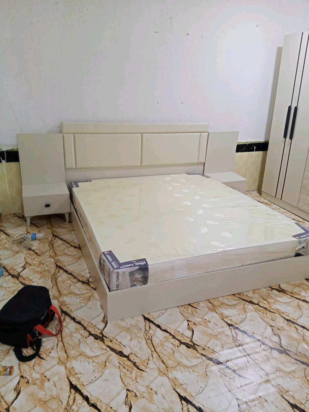 ​غرفة نوم كاملة بحالة ممتازة وتصميم عصري أنيق باللون الكريمي (البيج الفاتح) مع تطعيمات خشبية ناعمة ومقابض باللون الأسود المودرن.
​محتويات الغرفة:
​كشمير/كنتور (خزانة ملابس): 6 أبواب، بمساحة تخزين ممتازة، مجهز بمقابض طولية سوداء أنيقة تمنحه لمساً عصرية مميزة.
​سرير (جرباية): تصميم مودرن مع رأسية (تاج) مبطنة بجلد مريح، مدمج معها 2 كوميدي جانبي يحتوي كل منهما على درج تخزين.
​دوشق (مرتبة): جديد مغلف بالنايلون (صناعة تركية / Model Turkey).