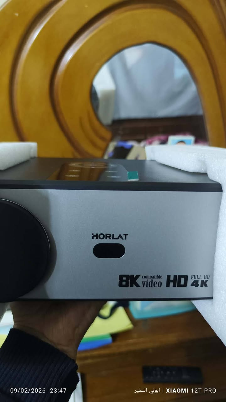 هذا الجهاز هو جهاز عرض فيديو (Projector) من علامة Horlat التجارية، وتحديداً الطراز Horlat T09 أو طرازات مشابهة مثل T3N. 
المميزات والمواصفات الرئيسية:
الدقة: يدعم دقة 1080p (Full HD) بشكل أصلي، مع القدرة على تشغيل محتوى فيديو بدقة 4K و 8K.
السطوع: يتميز بسطوع عالي يصل إلى 35,000 لومن في بعض الإصدارات، مما يجعله مناسباً لظروف إضاءة متنوعة.
النظام الذكي: يعمل بنظام تشغيل Android (غالباً الإصدار 12.0)، مما يتيح تحميل تطبيقات مثل Netflix و YouTube مباشرة على الجهاز.
الاتصال: يدعم الاتصال اللاسلكي عبر Wi-Fi 6 (بترددين 2.4G و 5G) وتقنية Bluetooth 5.1/5.3 لتوصيل السماعات الخارجية.
التحكم الآلي: يحتوي على ميزات ذكية مثل التركيز التلقائي (Auto Focus) وتصحيح انحراف الصورة التلقائي.
المنافذ: يضم منافذ متعددة تشمل 2×HDMI، وUSB، وAV، ومخرج صوت 3.5 مم. 
معلومات إضافية:
حجم العرض: يمكنه عرض صورة تتراوح بين 40 إلى 300 بوصة.
العمر الافتراضي: تعيش لمبة الـ LED الخاصة به لأكثر من 50,000 ساعة.


**إذا كنت صاحب هذا الإعلان وتريد حذفه لأي سبب، رجاءا أرسل رسالة إلى الدعم الفني**