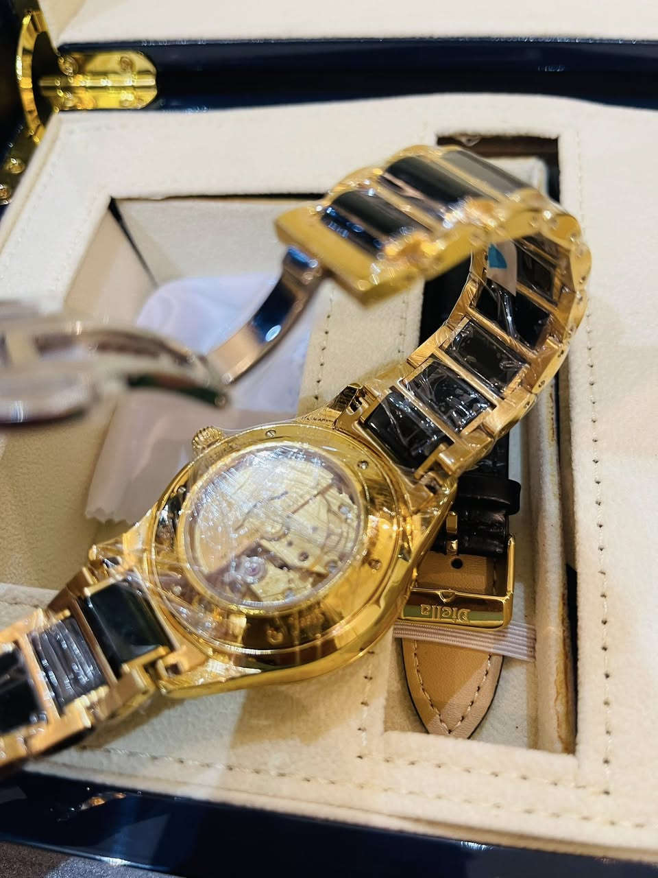 قطعه تحفه ساعه من ماركة Diella، وتحديداً موديل AD6008. تتميز هذه الساعة بتصميم فاخر يجمع بين الذهب واليشم (Jade) الأسود أو الأخضر الداكن، وهي ساعة أوتوماتيكية ميكانيكية لا تحتاج إلى بطارية. 
أبرز مواصفات الساعة:
الحركة: ميكانيكية أوتوماتيكية تعتمد على حركة المعصم لتوليد الطاقة.
المواد: مصنوعة من الفولاذ المقاوم للصدأ المطلي باللون الذهبي مع ترصيع باليشم الطبيعي في السوار والإطار.
المينا: يحتوي على أحجار الراين كعلامات للساعات، مع نافذة لعرض التاريخ عند الساعة الثالثة.
المقاومة للماء: مقاومة للماء حتى عمق 50 متراً (5ATM)، مما يجعلها مناسبة للاستخدام اليومي مثل غسل اليدين أو التعرض للمطر.
الزجاج: مرآة من زجاج الياقوت (Sapphire Glass) المقاوم للخدش. 
تأتي الساعة عادةً في صندوق فخم مع سوار إضافي من الجلد وأداة لتعديل طول السوار المعدني.


**إذا كنت صاحب هذا الإعلان وتريد حذفه لأي سبب، رجاءا أرسل رسالة إلى الدعم الفني**