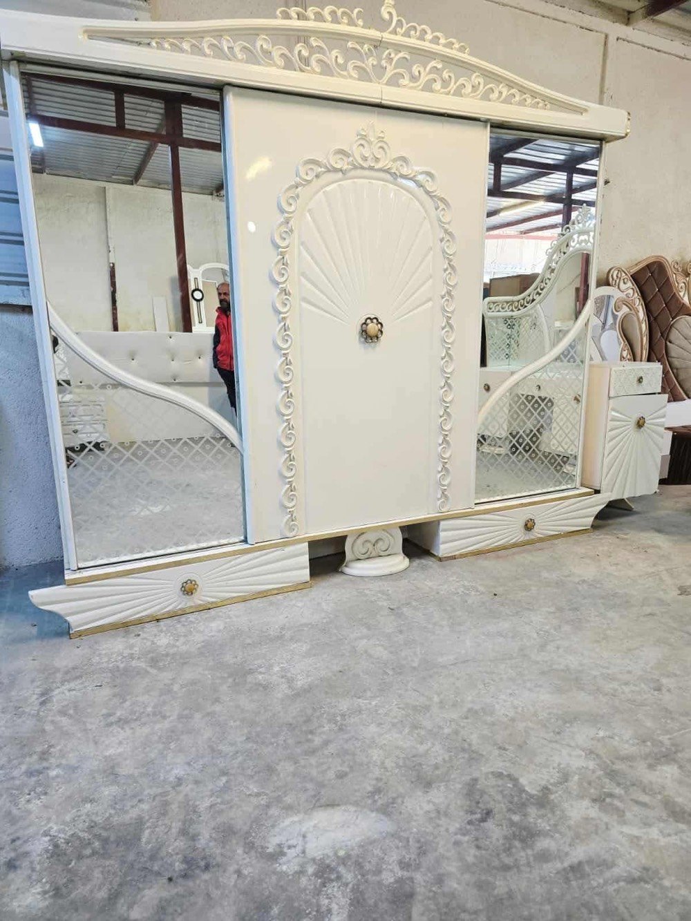 غرفة نوم فاخرة تصميم كلاسيكي، تتضمن سرير كبير مع خلفية منجدة بتفاصيل زخرفية جذابة باللون الأبيض، بالإضافة إلى خزانة ملابس مرايا وشيفونيرة مع أدراج واسعة. التصميم يتميز بالنقوش الكلاسيكية التي تضيف لمسة من الأناقة والرقي للغرفة. الأثاث بحالة جيدة ويضفي لمسة فاخرة على أي غرفة النوم.