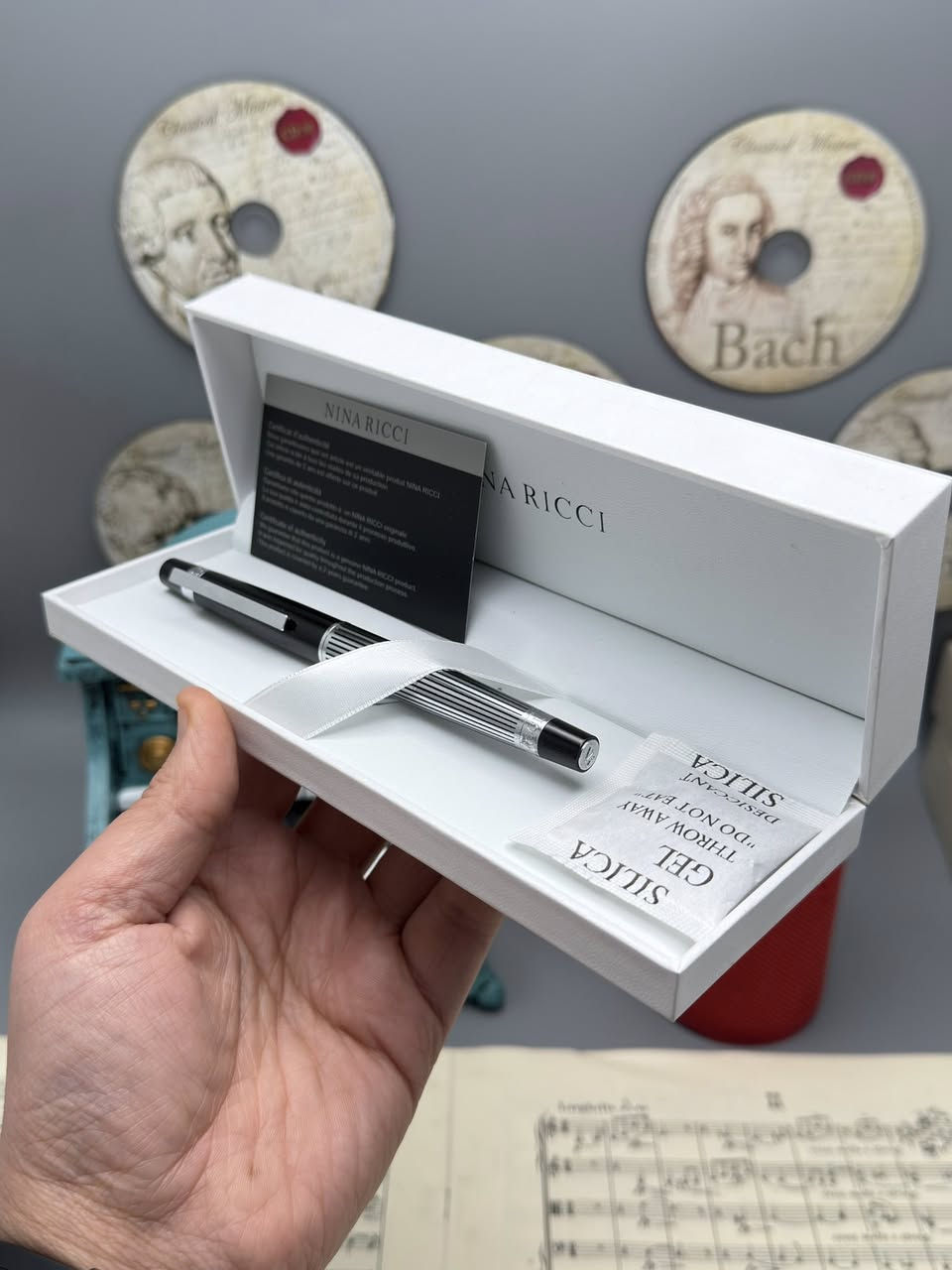 نينا ريتشي (Nina Ricci). هذه الأقلام تُعرف بكونها إكسسوارات فاخرة تجمع بين الأناقة الباريسية والعملية.
إليك شرح مفصل لما تظهره الصور:
1. العلامة التجارية والجودة
• الماركة: Nina Ricci هي دار أزياء راقية، وأقلامها تُصنف كأدوات كتابة "برستيج" (Prestige).
• الأصالة: يظهر في الصور "شهادة أصالة" (Certificate of Authenticity)، مما يؤكد أن القلم أصلي ويأتي مع ضمان (غالباً لمدة سنتين ضد عيوب التصنيع).
2. التصاميم والموديلات الظاهرة
من خلال الصور، نرى أربعة أشكال مختلفة، مما يوفر خيارات متنوعة للأذواق:
• القلم الأول (بني مموج): يتميز بنقشة "Tortoise" أو التورتويز (صدفة السلحفاة) الكلاسيكية مع لمسات معدنية داكنة. هذا التصميم يوحي بالفخامة التقليدية والمظهر الدافئ.
• القلم الثاني (أسود وفضي): تصميم كلاسيكي "مينيماليست" باللون الأسود اللامع مع حواف فضية، وهو مثالي لرجال الأعمال والمناسبات الرسمية.
• القلم الثالث (ذهبي مخطط): قلم باللون الذهبي الكامل مع خطوط طولية محفورة، يعطي طابعاً ملكياً لافتاً للنظر.
• القلم الرابع (فضي/كروم مخطط): مشابه للذهبي ولكن باللون الفضي، يتميز بالهدوء والعصرية، ومقاوم بشكل جيد للخدوش بفضل المادة المعدنية.
3. المواصفات الفنية
• نوع القلم: يظهر من الرؤوس أنها أقلام حبر جاف (Ballpoint) تعمل غالباً بآلية التدوير (Twist mechanism) لفتح وإغلاق القلم.
• الخامات: الهيكل عادة ما يكون مصنوعاً من النحاس المطلي بالروديوم، الذهب، أو الورنيش عالي الجودة (Lacquer).
• التغليف: يأتي في علبة بيضاء فاخرة مبطنة من الداخل بكلمة "NINA RICCI" مطبوعة بشكل أنيق، مما يجعله خياراً ممتازاً للهدايا.
4. مميزات الاقتناء
• الوزن: هذه الأقلام تمتاز بوزن متزن (ليست خفيفة جداً ولا ثقيلة)، مما يوفر راحة أثناء الكتابة الطويلة.
• سهولة التعبئة: تستخدم عبوات حبر قياسية متوفرة بسهولة في المكتبات الكبرى.
• القيمة: يعتبر قطعة إكسسوار تكمل المظهر الشخصي، تماماً مثل الساعة أو المحفظة.

للحجز والاستفسار 
***********
