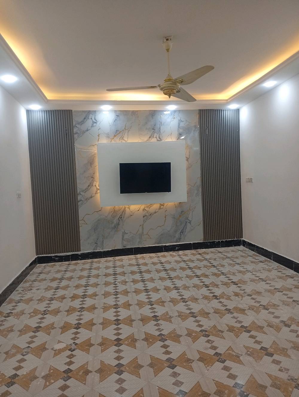 غرفة استقبال حديثة للبيع، تتميز بتصميم عصري أنيق مع إضاءة مخفية وجدارية رخامية تعطي لمسة فاخرة للديكور. الأرضية مزينة ببورسلين عالي الجودة بلون جذاب. الغرفة تحتوي على مروحة سقف لضمان التهوية الجيدة.