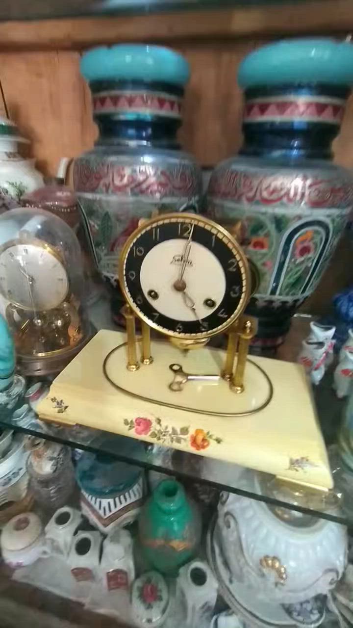 ساعة مكتبية أو رفّية (Mantel/Table Clock) كلاسيكية مميزة.  
​العلامة التجارية:   اسم الساعه "Selva"، وهي علامة تجارية ألمانية معروفة جداً في مجال قطع غيار الساعات، ومجموعات تركيب الساعات، والساعات الميكانيكية التقليدية بجودة عالية.
​المنشأ:  أسفل الرقم 6 عبارة صغيرة  مكتوب "Made in Germany" (صنع في ألمانيا)، وهو أمر متوافق تماماً مع العلامة التجارية Selva.
​ التصميم والهيكل
​القبة الزجاجية (Glass Dome): الساعة مغطاة بقبة زجاجية شفافة منحنية (تُعرف بساعات القبة أو ساعات الذكرى السنوية أحياناً، وإن كانت هذه تعمل ببندول تقليدي وليس بندولاً دواراً). وظيفتها حماية الآلية الداخلية والميناء من الأتربة.
​الميناء (Dial): يتميز بتصميم ثنائي اللون (حلقة خارجية سوداء تحتوي على أرقام عربية مذهبة واضحة، ومركز دائري بلون كريمي/أبيض مطفأ).
​الأعمدة والقاعدة: ترتكز الساعة على أعمدة نحاسية مضلعة مذهبة فوق قاعدة بيضاء أو كريمية المزينة بنقوش وردية ناعمة مرسومة باليد، مما يعطيها طابعاً أنثوياً أو ريفياً كلاسيكياً (Shabby Chic / Vintage style).
​الآلية والتشغيل (الميكانيكا)
​المفاتيح وثقوب التعبئة: يحتوي الميناء على ثقبين للتعبئة (Winding holes) بجانب الرقمين 4 و 8. هذا يعني أن الساعة تحتوي على نابضين (زُنبركين): واحد لتشغيل حركة عقارب الساعة، والآخر مخصص لآلية الرنين (الدق أو الجرس).
​مفتاح التعبئة:  مفتاح التعبئة المعدني الأصلي مستلقياً على قاعدة الساعة داخل القبة الزجاجية.
​البندول (Pendulum): بندول نحاسي لامع أسفل الميناء، وهو المسؤول عن تنظيم الوقت عبر حركته الاهتزازية يميناً ويساراً.
​ الحالة العامة  الساعة في حالة جيدة جداً ونظيفة. النحاس يحتفظ بلمعانه، والزجاج سليم لا تظهر فيه شروخ واضحة، والرسومات على القاعدة بحالة ممتازة.
​القيمة: هذا النوع من الساعات يجمع بين القيمة الوظيفية والجمالية كقطع ديكور "أنتيك" أو عتيقة مرغوبة لمحبي الساعات الألمانية الميكانيكية.


**إذا كنت صاحب هذا الإعلان وتريد حذفه لأي سبب، رجاءا أرسل رسالة إلى الدعم الفني**